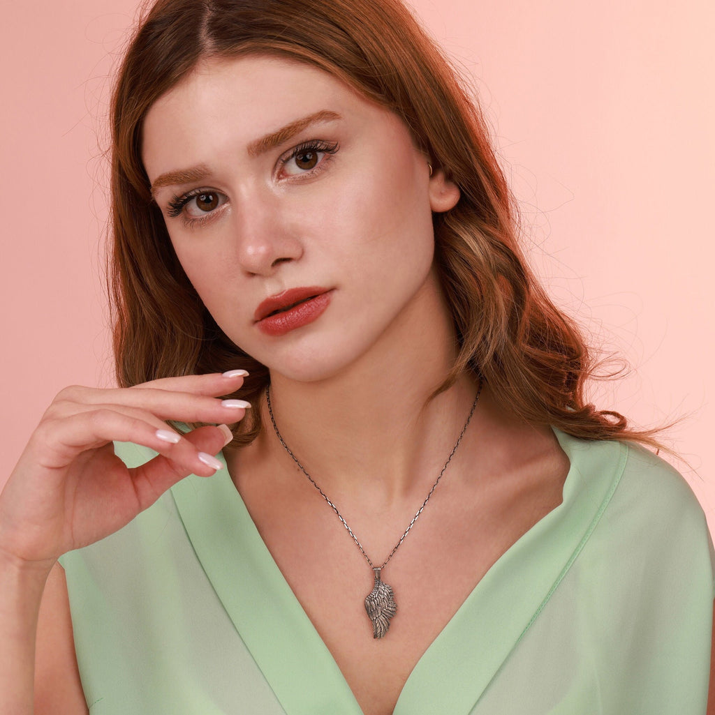Woman wearing an oxidized sterling silver angel wing necklace against a pink background