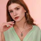 Woman wearing an oxidized sterling silver angel wing necklace against a pink background