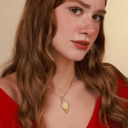 Woman wearing a gold necklace with a wing pendant against a beige background