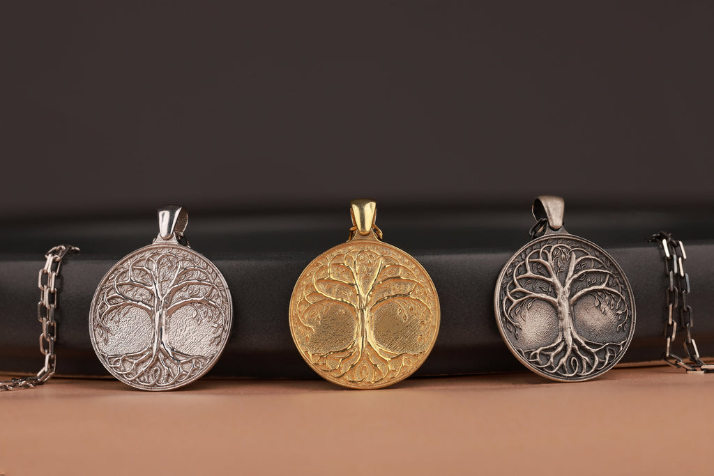 Three tree of life pendants in polished silver, gold, and oxidized silver on a dark background