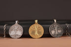 Three tree of life pendants in polished silver, gold, and oxidized silver on a dark background