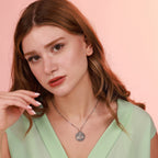 Woman wearing a green top and an oxidized necklace with a detailed tree of life pendant against a pink background
