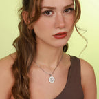 Woman wearing a necklace with a circular pendant against a light green background