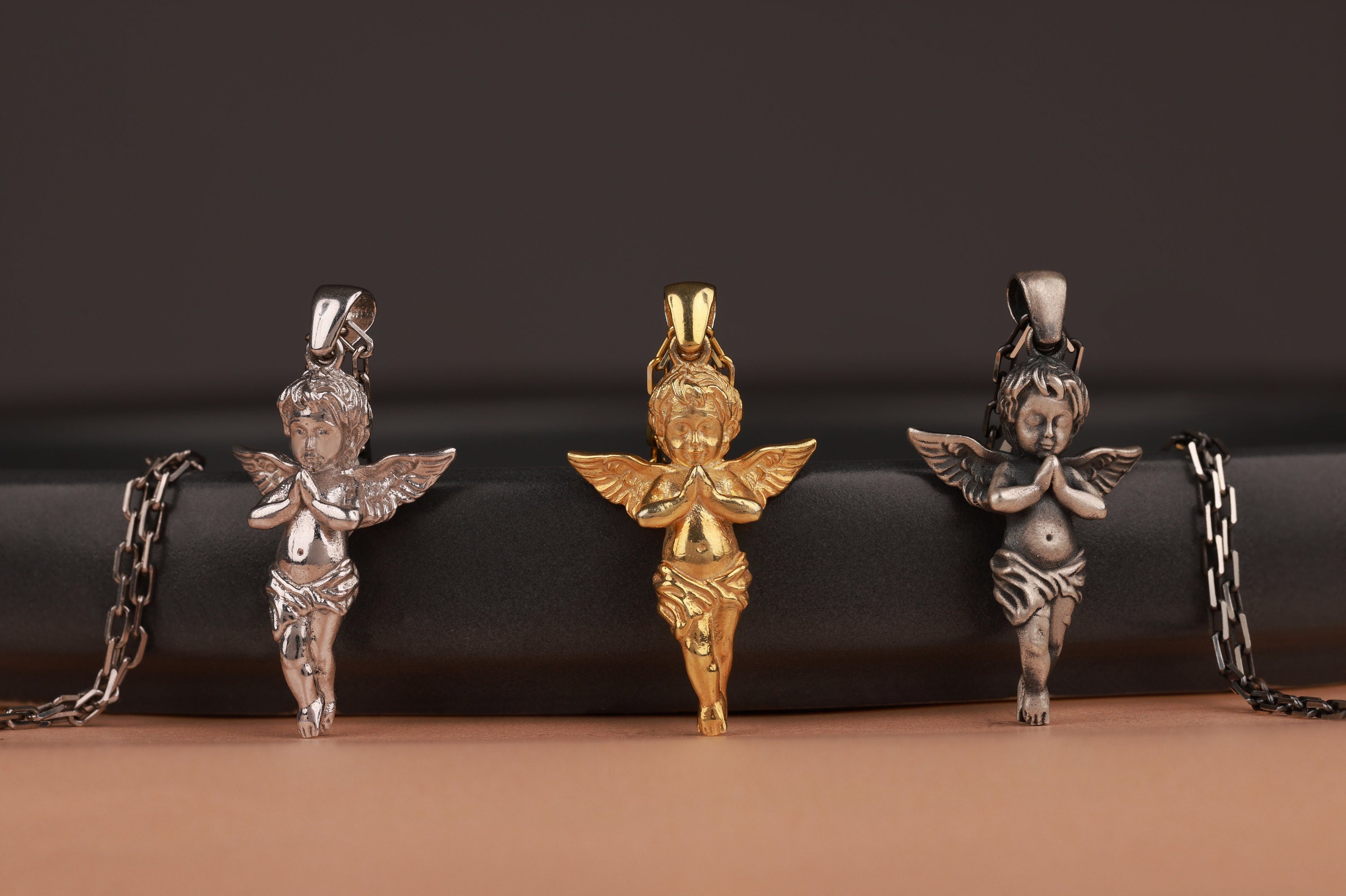 Three sculptural angel-shaped pendants on chains against a dark background