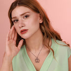 Woman wearing a green top and oxidized silver vitruvian man necklace against a pink background