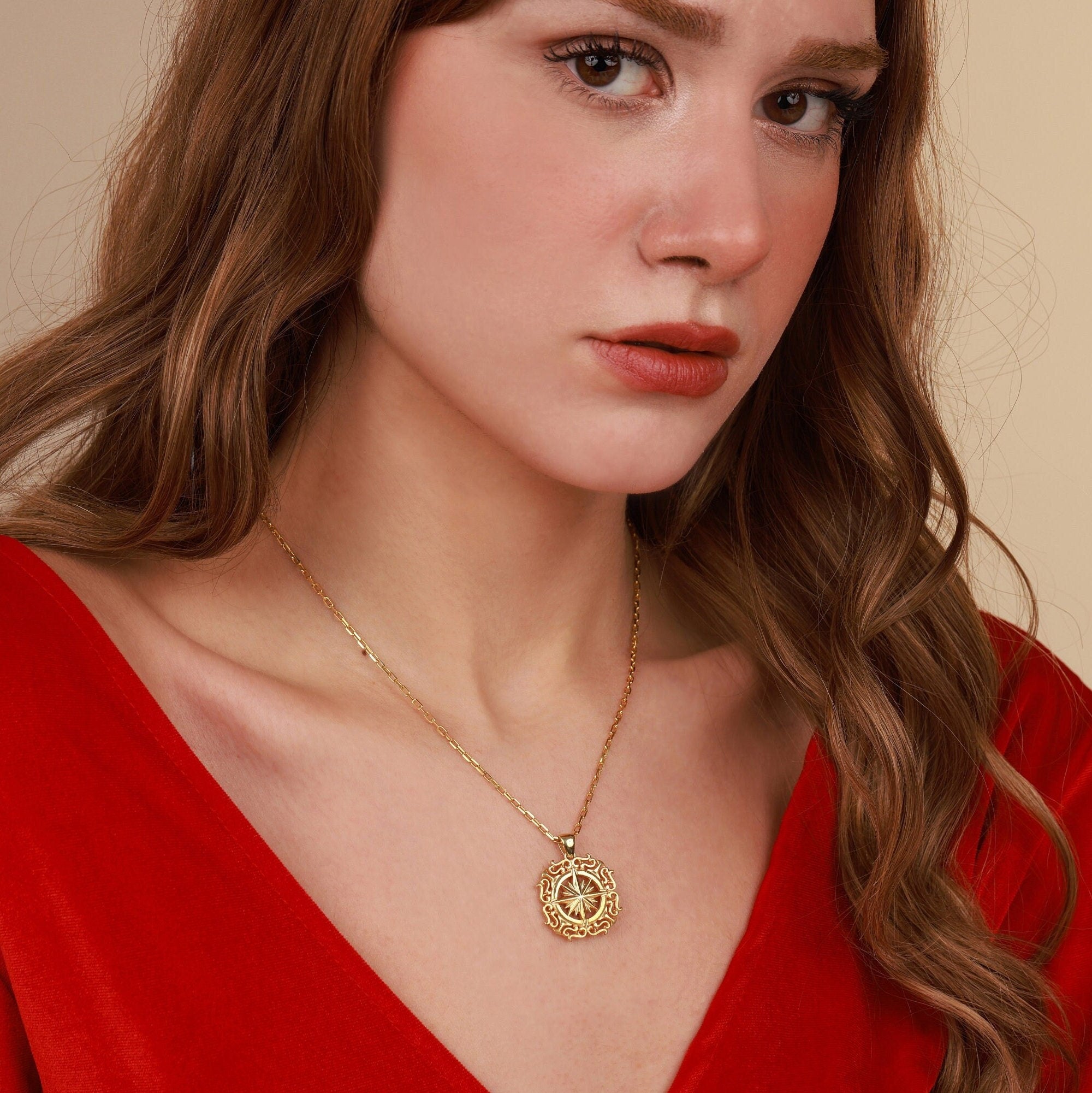 Woman wearing a gold north star necklace with a red top against a beige background