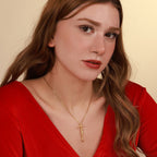 Woman wearing a red top and a gold necklace with a crucifix cross pendant against a beige background
