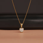 Gold necklace with a heart-shaped opal pendant on a brown background