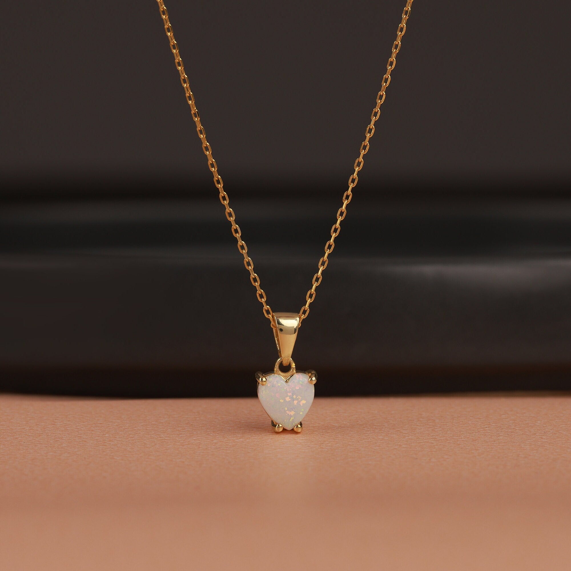 Gold necklace with a heart-shaped opal pendant on a brown background