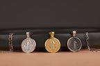 Three st benedict coin pendants on chains against a dark background