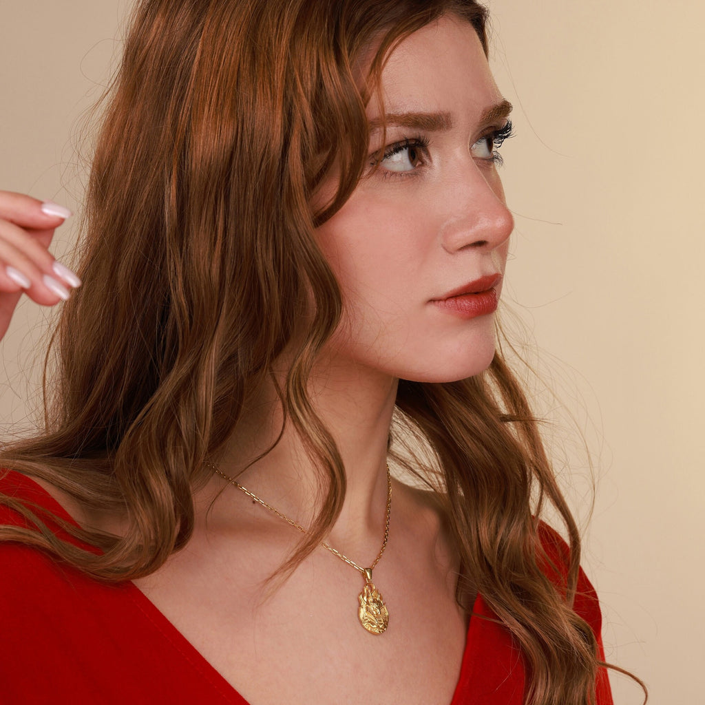 Woman wearing a gold necklace with a pendant against a beige background
