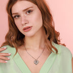 Woman wearing a silver heart-shaped necklace against a pink background