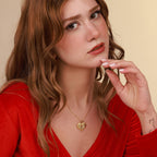 Woman wearing a gold necklace with a heart-shaped pendant of a horse against a beige background