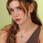 Woman wearing a silver necklace with a detailed pendant against a light green background