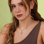 Woman wearing a sterling silver polished necklace with a flower cross pendant against a green background