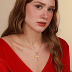 Woman wearing a gold necklace with a sword pendant against a beige background