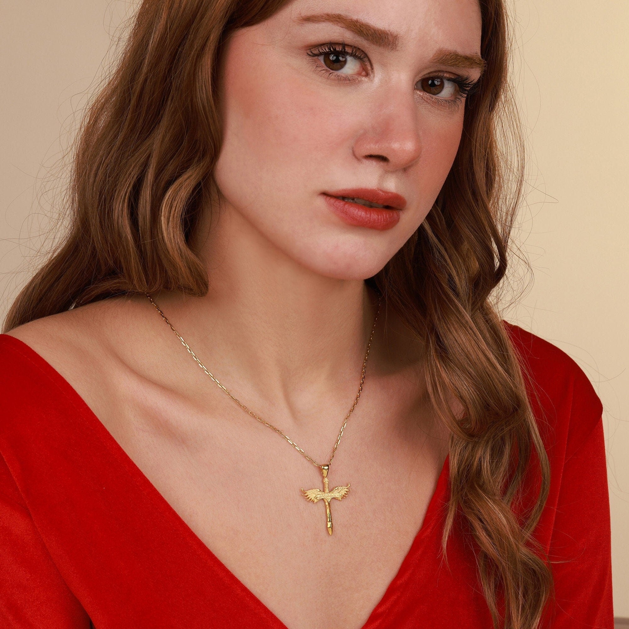 Woman wearing a gold necklace with a sword pendant against a beige background