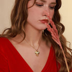 Woman wearing a gold necklace with an elephant head pendant, holding a dried flower against a beige background