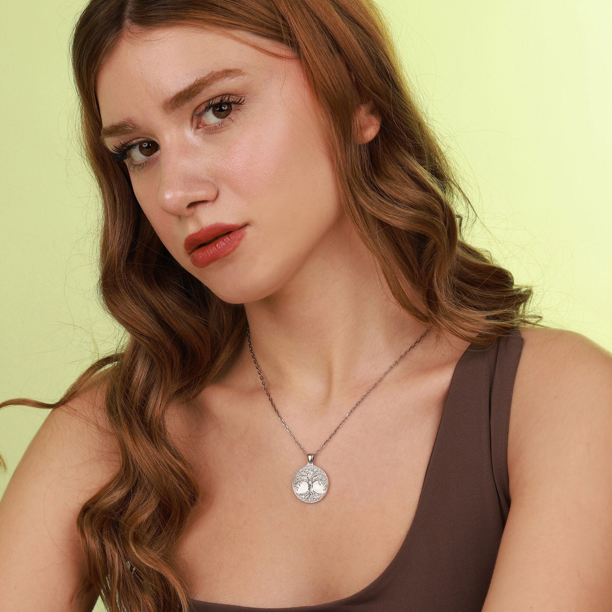 Woman wearing a polished sterling silver necklace with a tree of life pendant against a light green background
