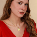 Woman wearing a gold necklace with a pendant against a neutral background