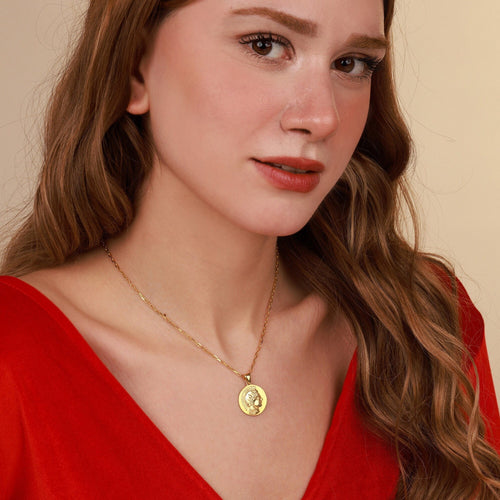 Woman wearing a gold necklace with a pendant against a neutral background