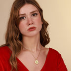 Woman wearing a red top and gold necklace against a beige background