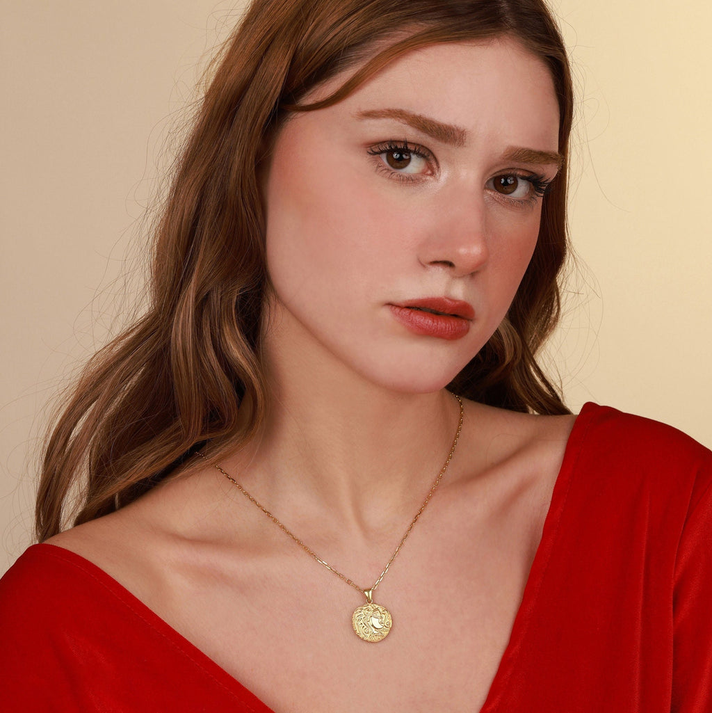 Woman wearing a gold necklace with a pendant against a beige background