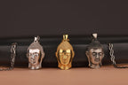 Three Buddha head pendants on chains against a dark background