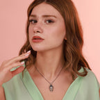 Woman wearing an oxidized silver necklace with a Buddha pendant against a pink background