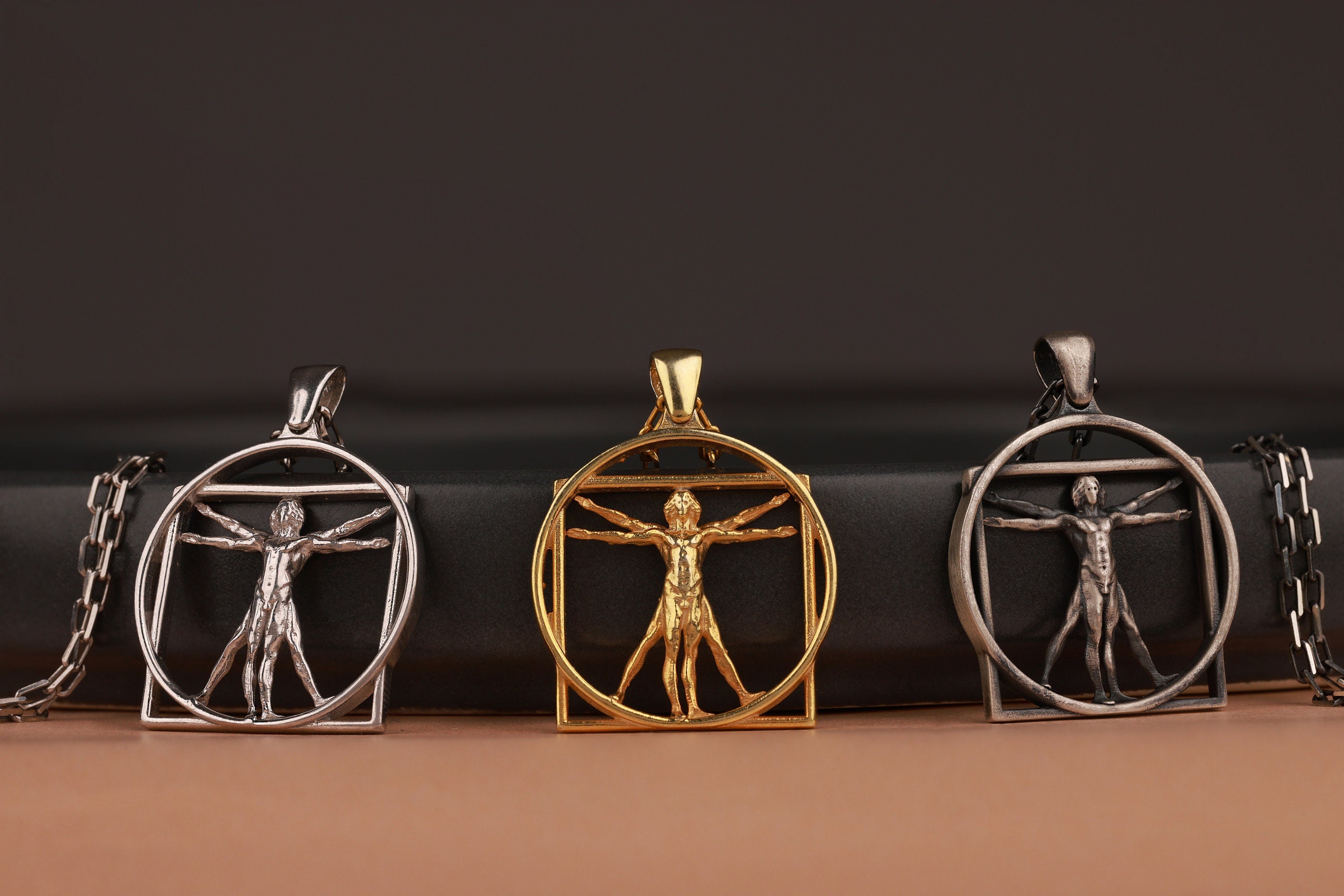Three pendants featuring the Renaissance Art Vitruvian Man design on a dark background