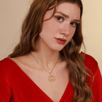 Woman wearing a gold vitruvian man necklace with a red top against a beige background