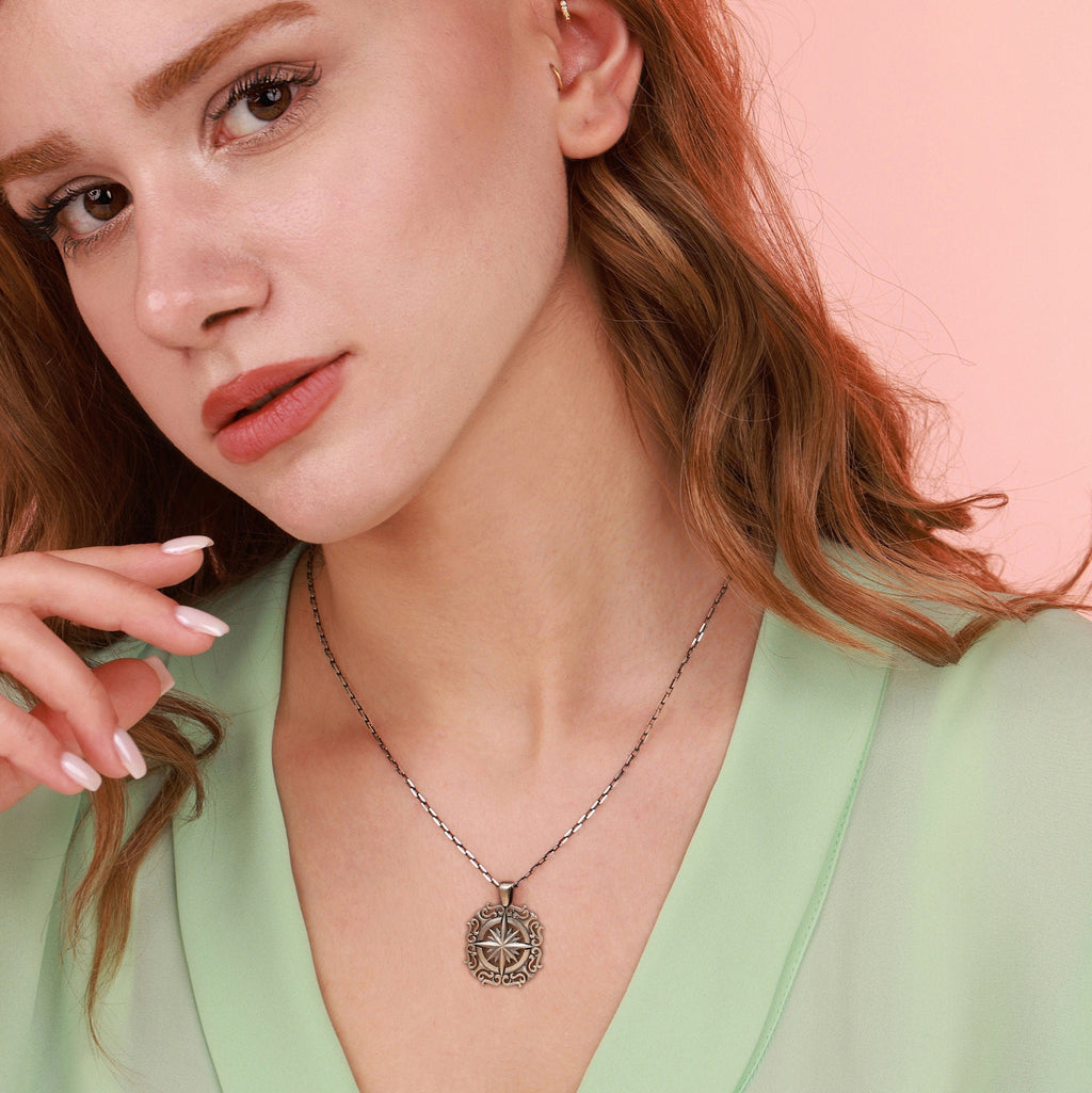 Close-up of a woman wearing an oxidized silver north star necklace with a pink background