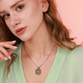 Close-up of a woman wearing an oxidized silver north star necklace with a pink background