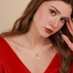 Woman wearing a gold necklace with a whale tail pendant against a beige background
