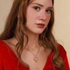 Woman wearing a gold mythological necklace with a pendant against a beige background