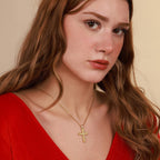 Woman wearing a gold vermeil necklace with a floral cross pendant against a beige background