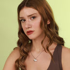 Woman wearing a necklace with a polished silver pendant against a light green background