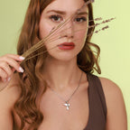 Woman wearing a necklace with a pigeon pendant in sterling silver, holding dry grass against her face on a light green background