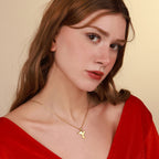 Woman wearing a gold dove necklace with a red top against a beige background