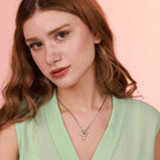 A woman wearing a green top and an oxidized sterling silver hummingbird necklace with a pink background