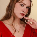 Woman wearing a gold hummingbird necklace with a red top against a beige background