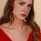Woman wearing a gold necklace with an egyptian pendant against a beige background