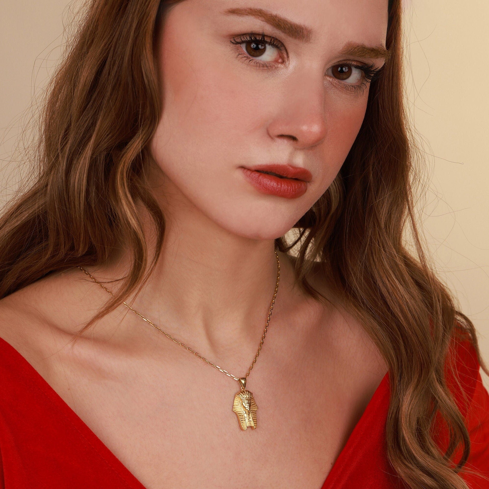 Woman wearing a gold necklace with an egyptian pendant against a beige background
