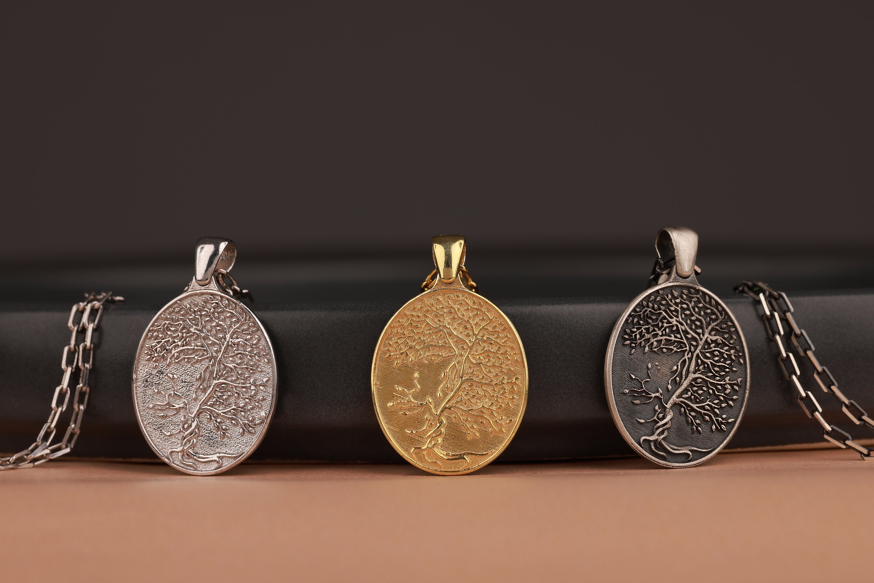 Three tree of life themed pendants on a black and brown background
