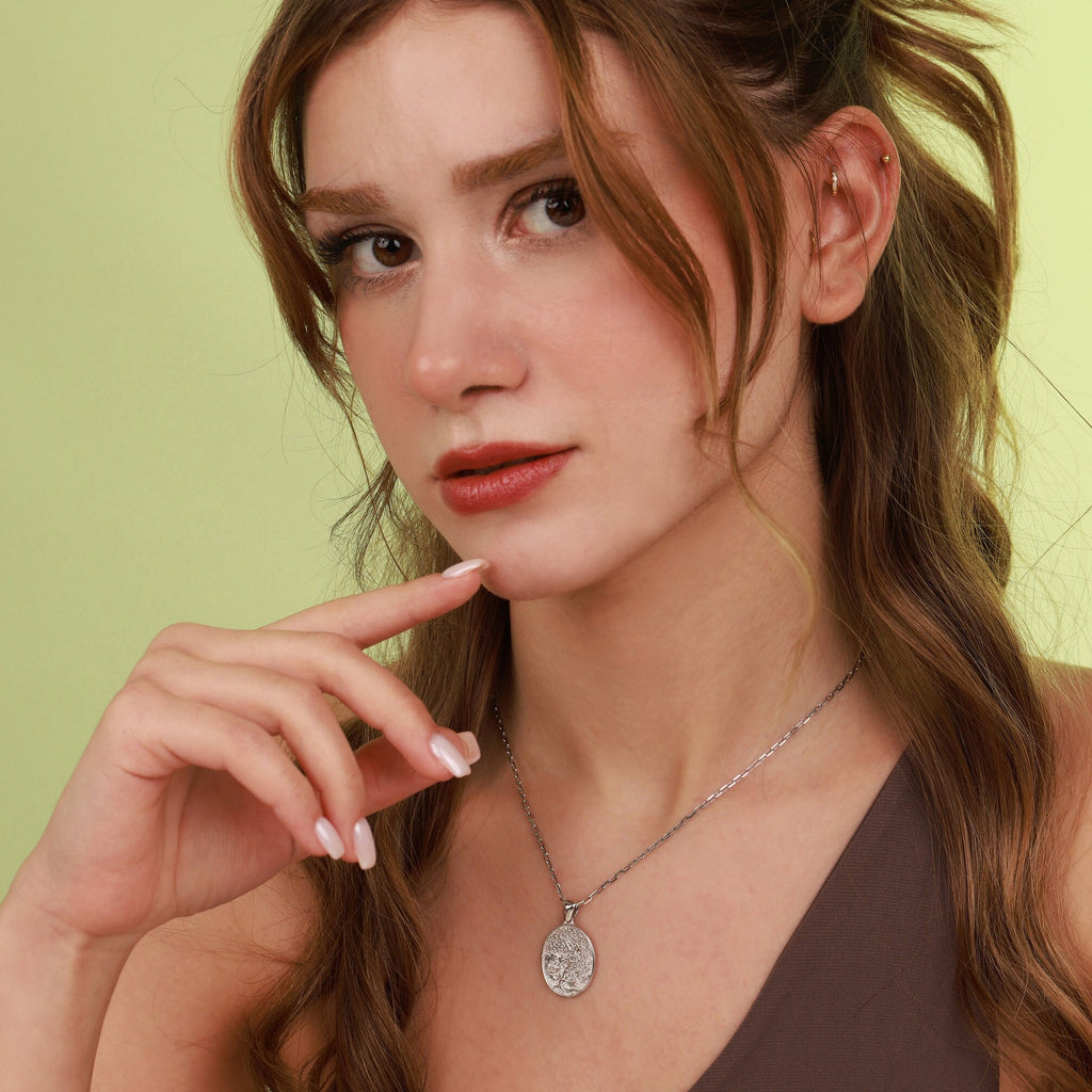 Woman wearing a polished necklace with a tree of life pendant against a light green background