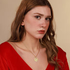 Woman wearing a gold necklace with a coin pendant against a beige background