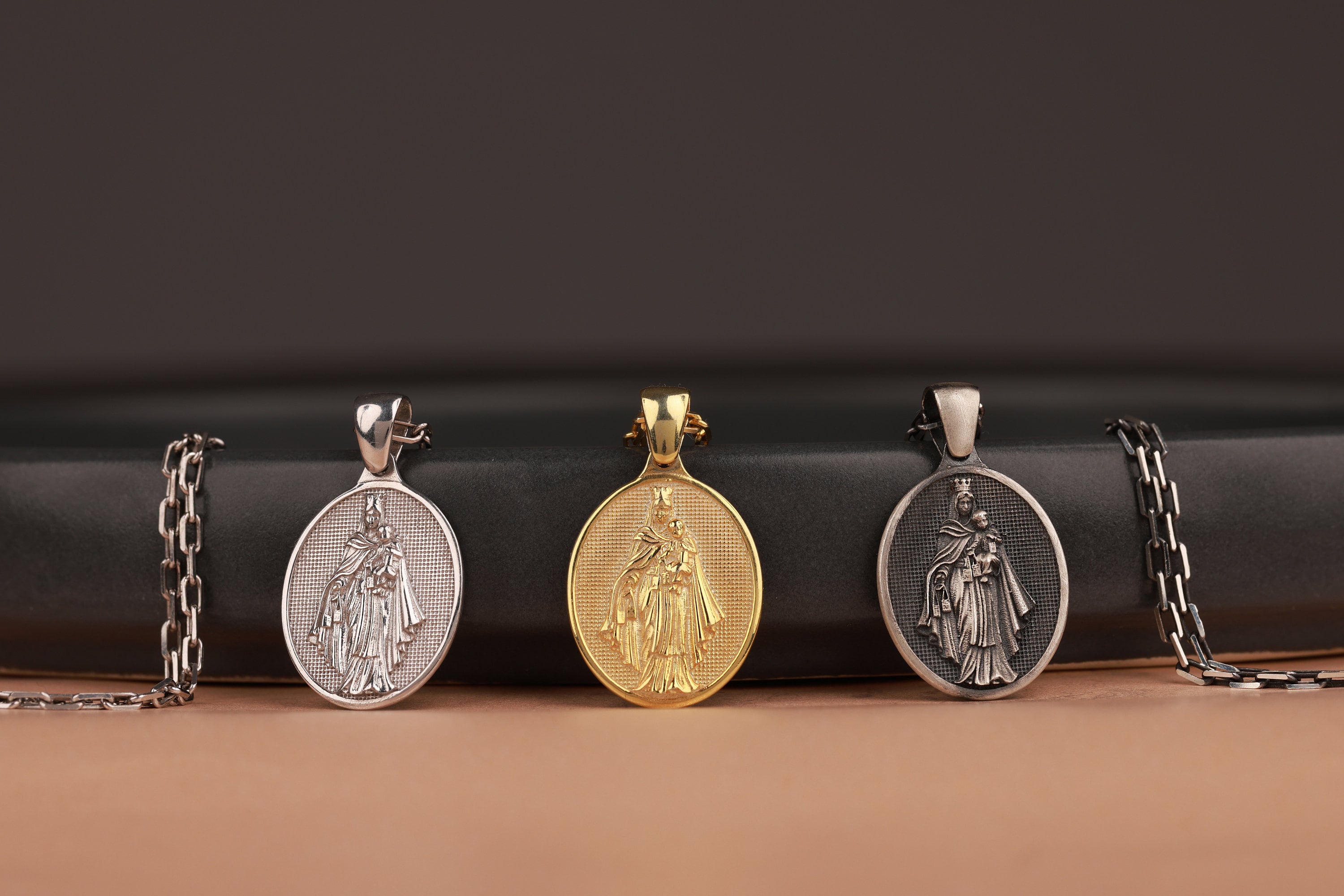 Four virgin mary pendants on chains against a dark background