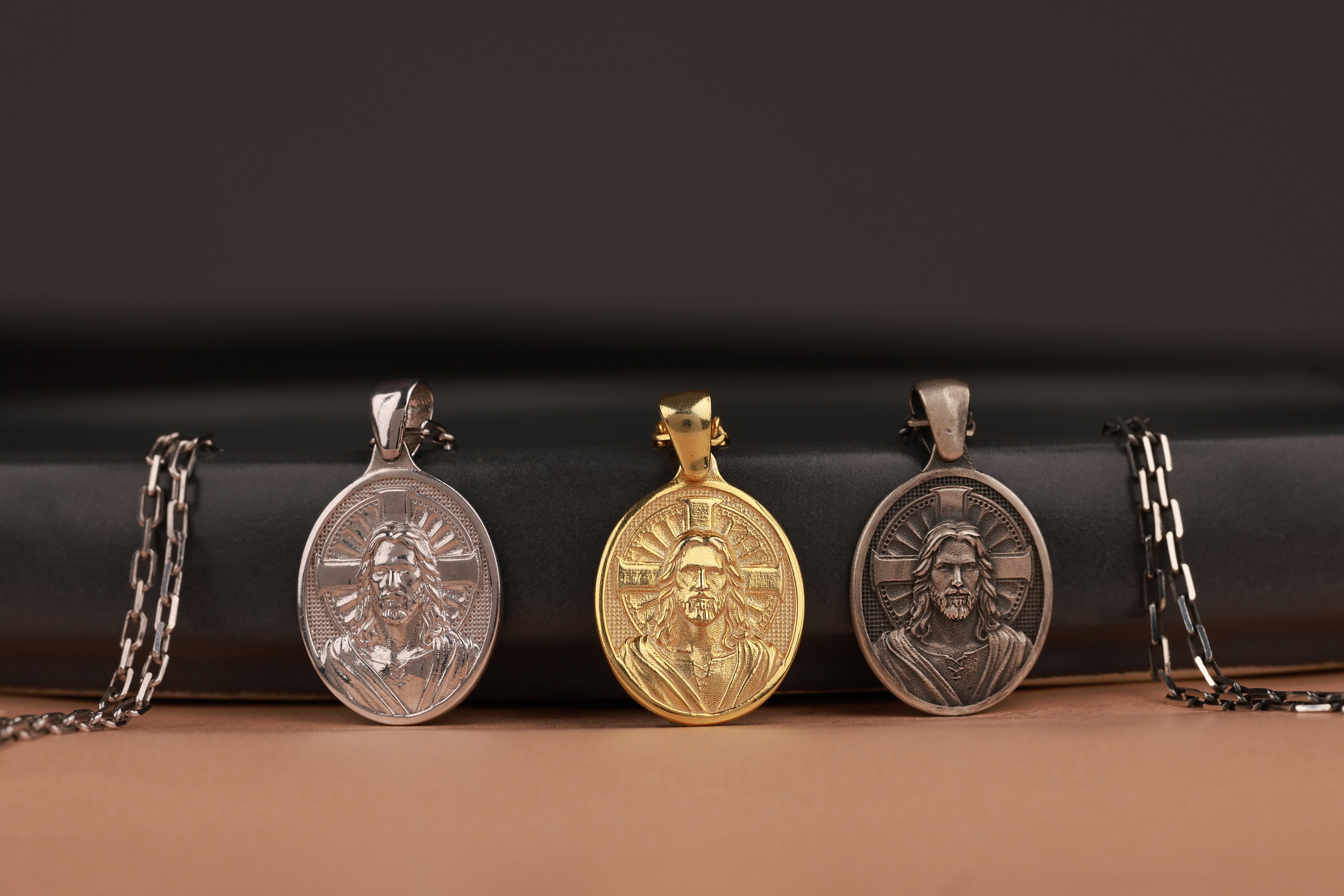 Four Jesus Christ pendants with different materials on a black and brown background