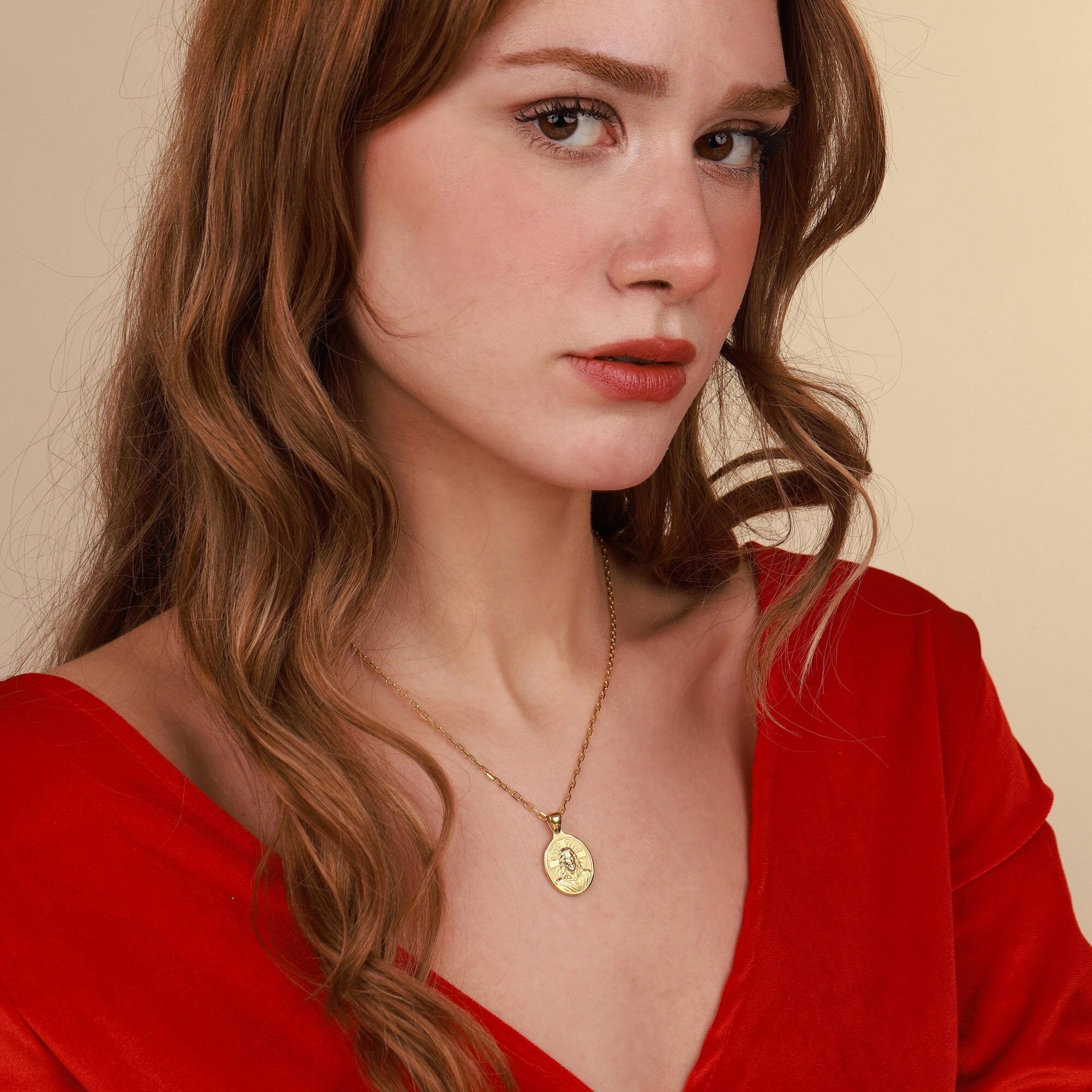 Woman wearing a gold faith necklace with a pendant against a beige background
