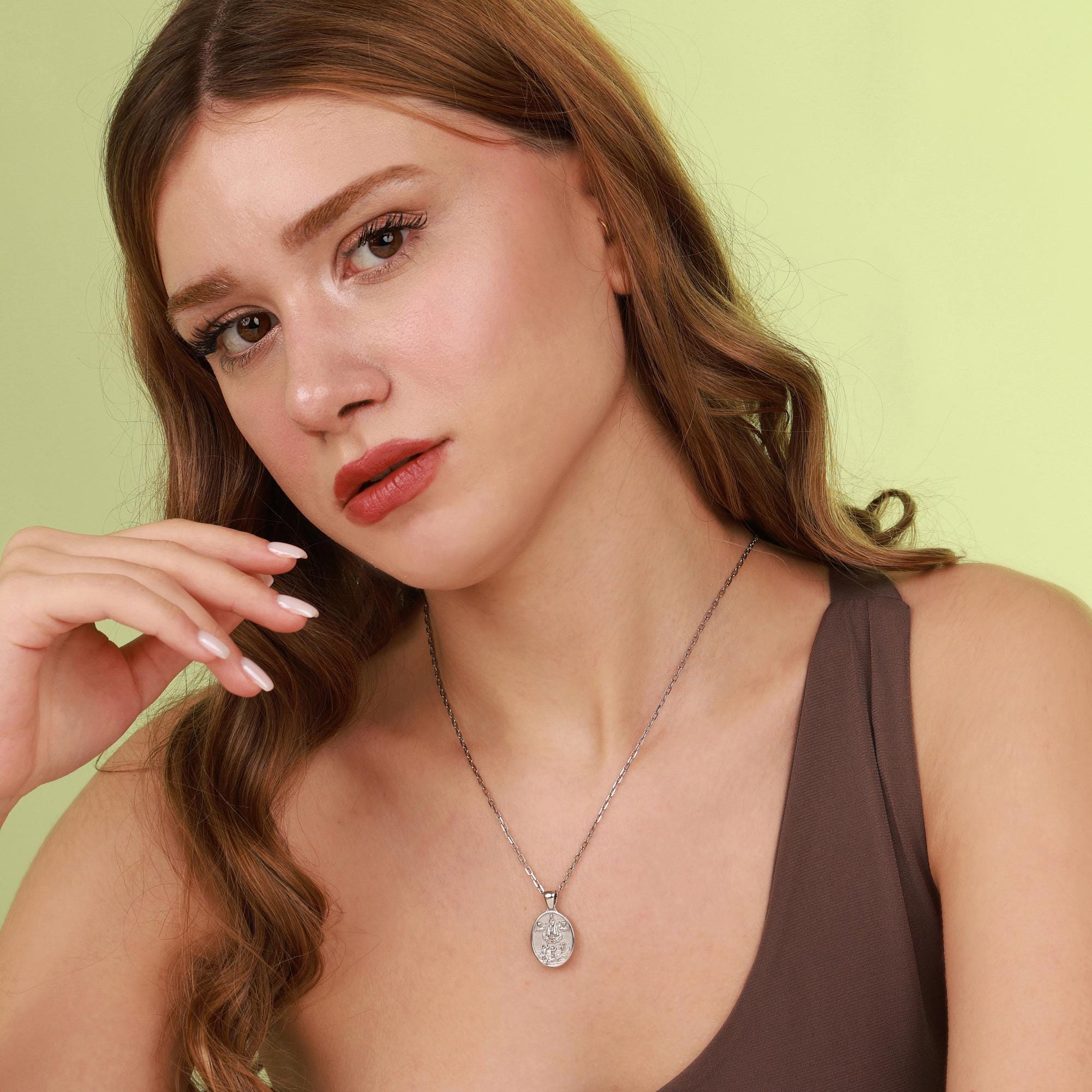 Woman wearing a necklace with a mother mary pendant against a light green background